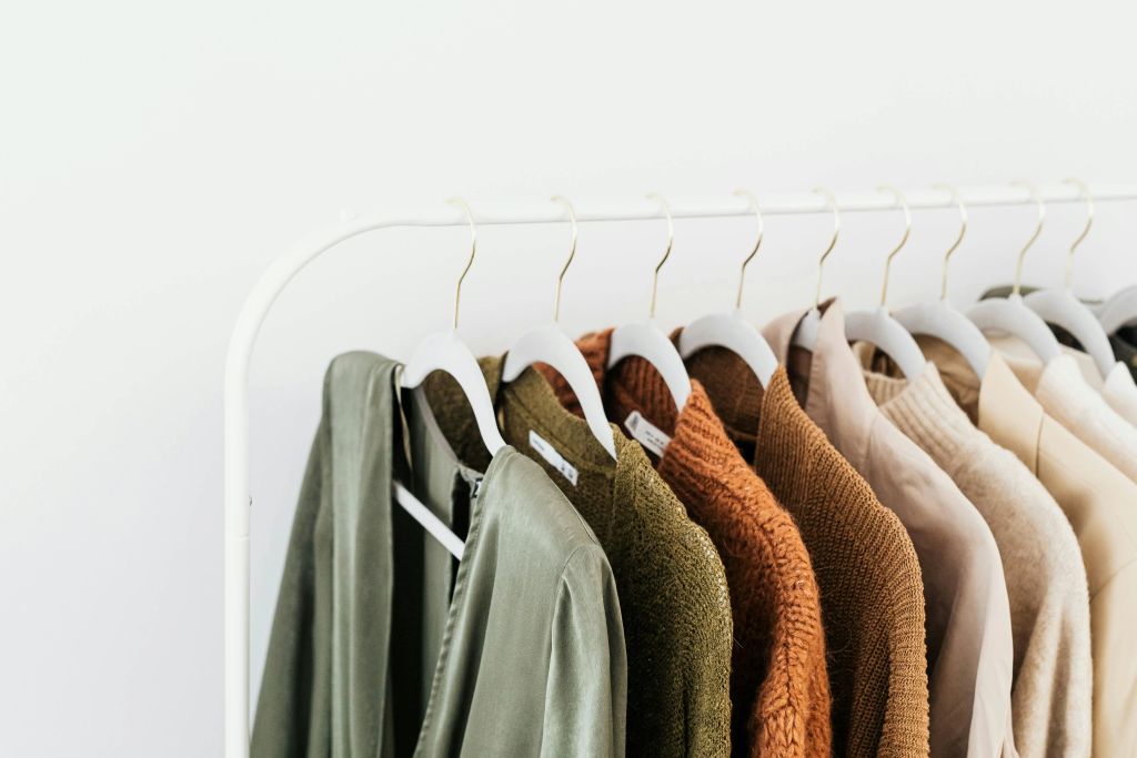 Netjes opgehangen kleding in natuurlijke tinten op een minimalistisch kledingrek, perfect voor een georganiseerde garderobe.